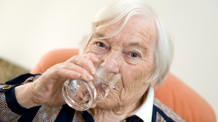 Senior pije wodę by uniknąć odwodnienia. 